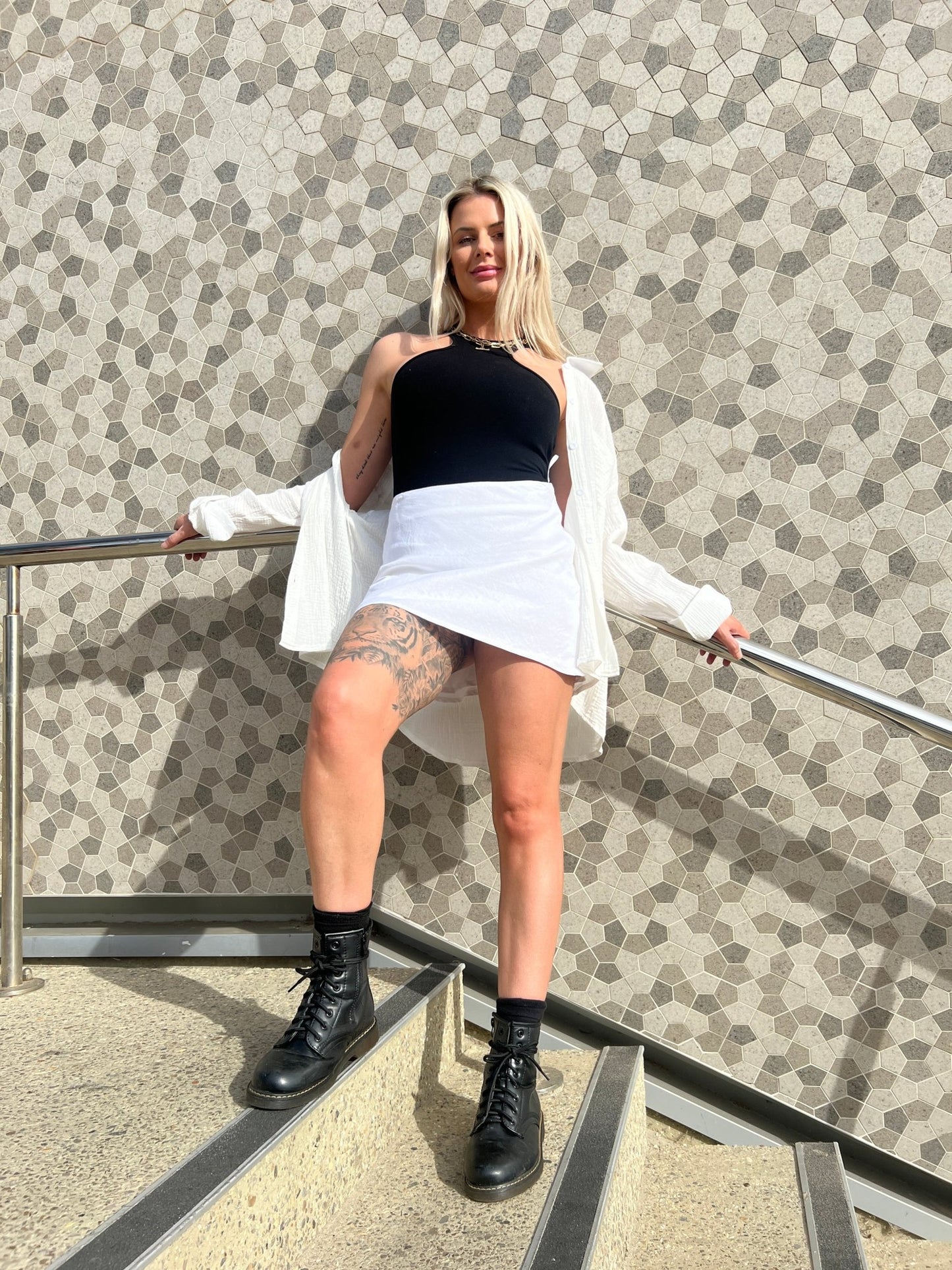 MOSS The Label black bodysuit worn with white skirt and boots standing on stairs against patterned wall