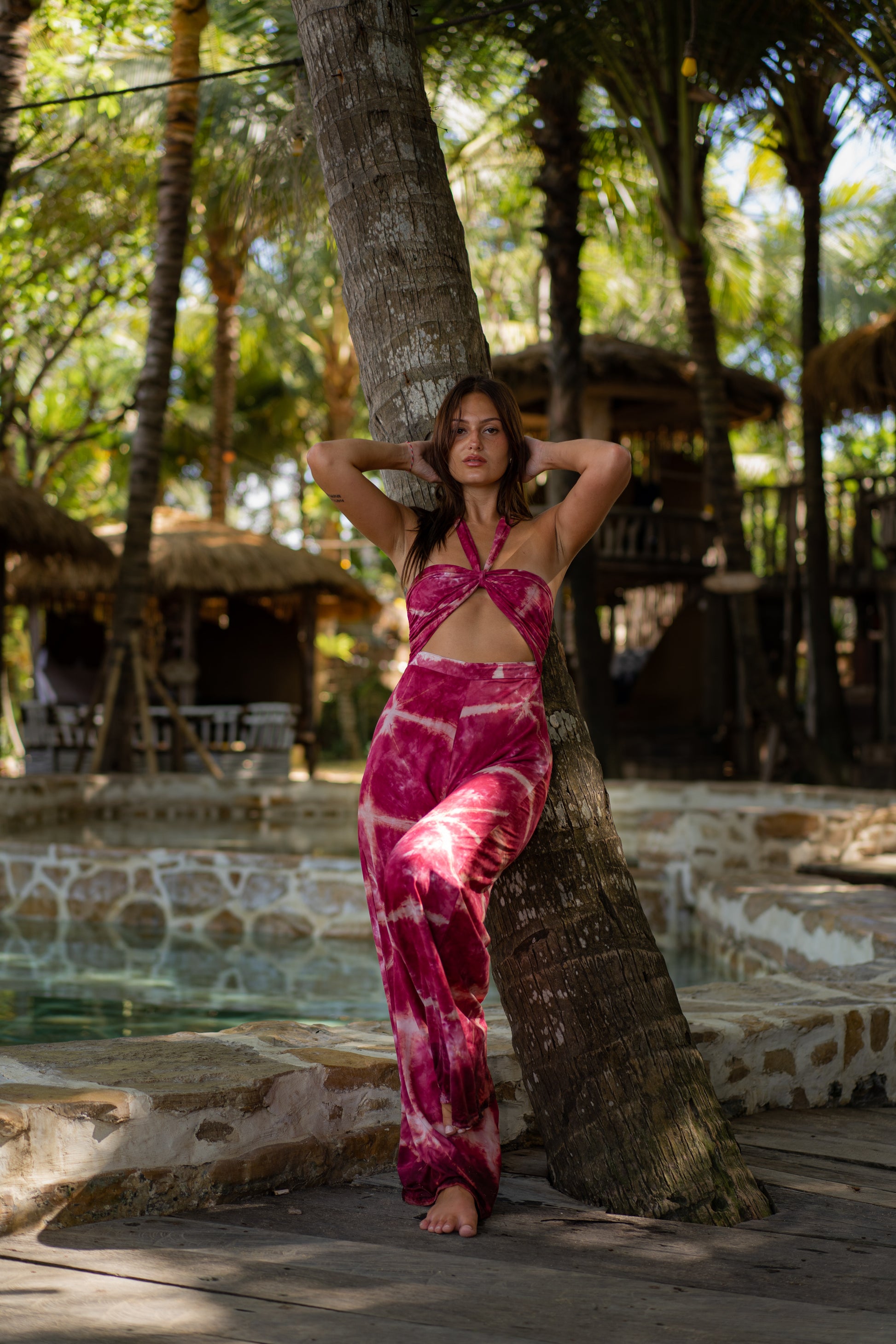 MOSS The Label vibrant pink tie-dye jumpsuit with cutout design worn by model leaning on palm tree
