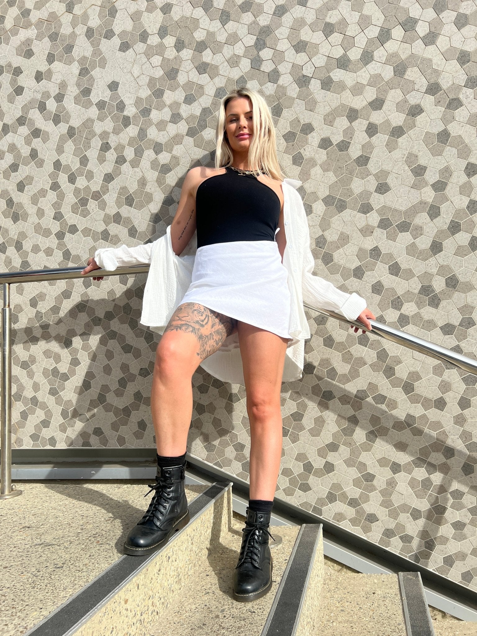 MOSS The Label black bodysuit worn with white skirt and boots standing on stairs against patterned wall